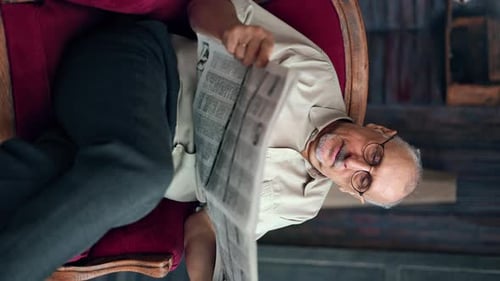 Senior Man Reads Newspaper in Red Chair
