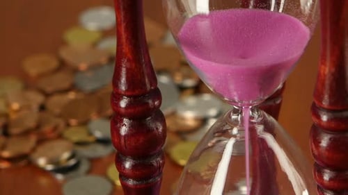 Hourglass on Coins Background. Close Up