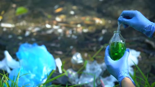 Ecologist in Gloves Taking Sample From Bottle Against Polluted Lake Background