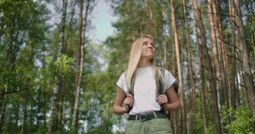 Handheld Shot of Thoughtful Serious Female Hiker with Backpack Walking Amidst Trees in Forest. A