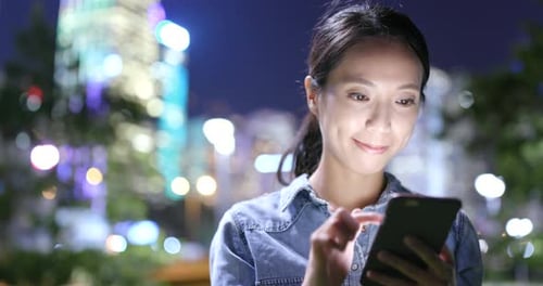 Femme envoyant un SMS sur un téléphone portable dans la ville la nuit