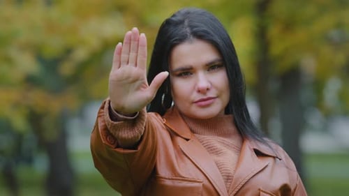 Serious Young Hispanic Girl Standing Outdoors Holds Out Palm Showing Stop Gesture Looking at Camera