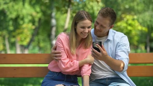Happy Couple Spending Time Together in Park Watching Photos on Smartphone, Date