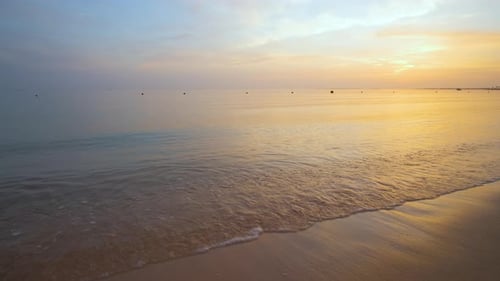 Calm sea shore with crushing waves on sandy beach at sunrise.
