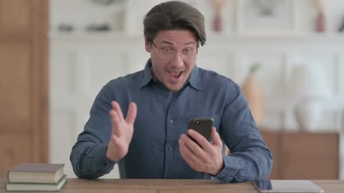 Excited Man Using Smartphone at a Desk
