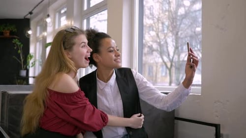 Two Young Women Taking Selfies Together in Cafe