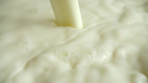 Ein fließender Milchstrahl in die milchige Oberfläche. Zeitlupe.