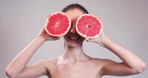 Menina escondendo os olhos com fatias de toranja