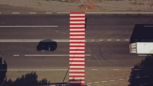 White truck and some cars passing the pedestrian crossing painted with red and white stripes