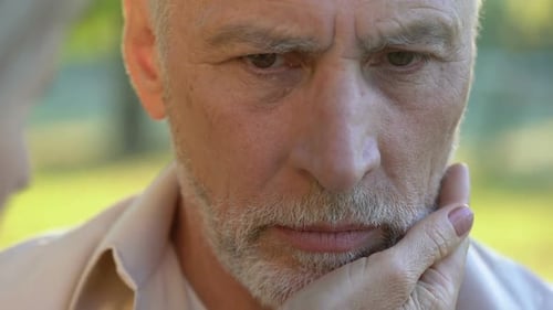 Sad Retired Man Looking Into Camera, Woman Supporting Husband, Close-Up View