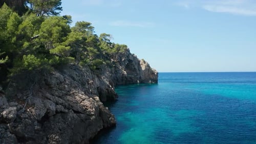 Drone Flight Over Rocky Coastline With Trees And Blue Tranquil Sea