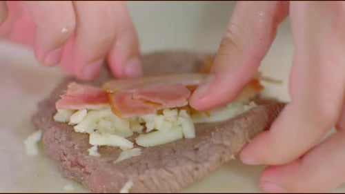 Hands assemble meat cheese and bacon dish