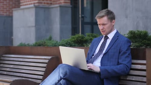 Man in Suit Using Laptop on Bench Outdoors