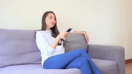 Woman Sitting on Couch Uses Remote Control