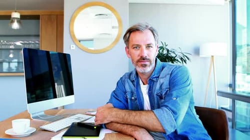 Man Smiling at Desk with Computer and Tablet