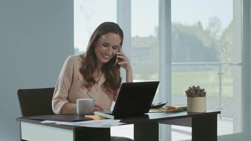 Woman on Phone Working at Desk with Laptop