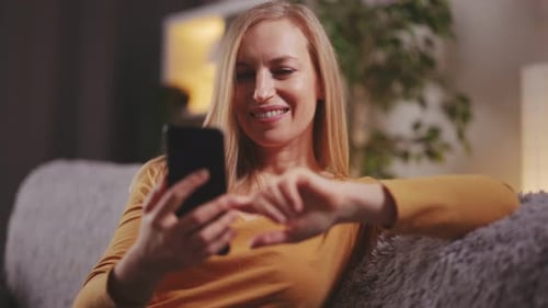 Woman Smiling, Using Phone on Couch Indoors