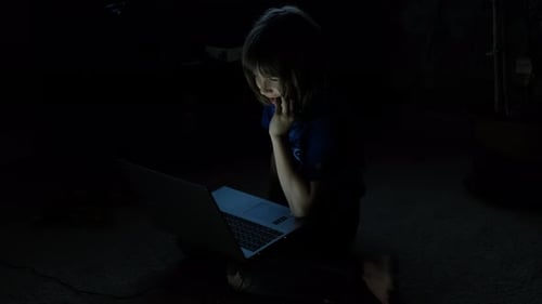 Nahaufnahme eines kleinen Jungen, der nachts mit einem Laptop im Internet auf dem Boden sitzt