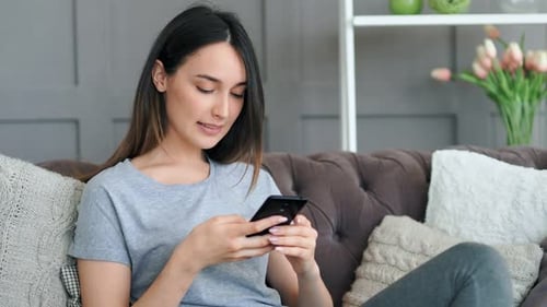 Woman Using Smartphone Relaxing on Sofa at Home