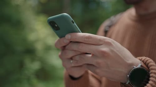 Closeup of a Mobile Phone in the Hands of a Male Traveler Walking Through the Forest