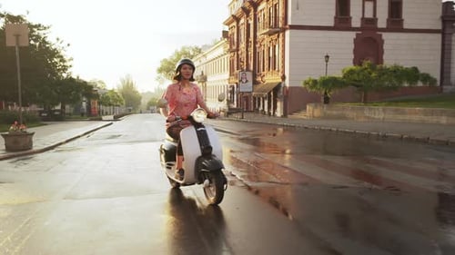 Junges schönes Mädchen fährt bei Sonnenaufgang mit dem Roller durch die Stadt