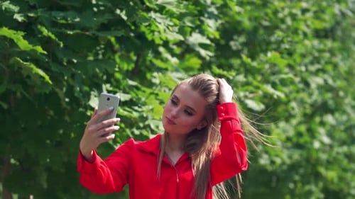 Pretty girl doing selfie outdoors. Sexy woman posing on her cell phone on the green tree background