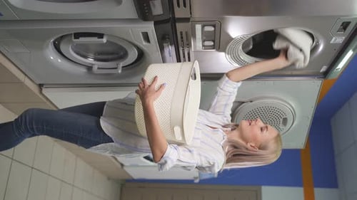 Woman Loads Laundry Into Washing Machine at Laundromat