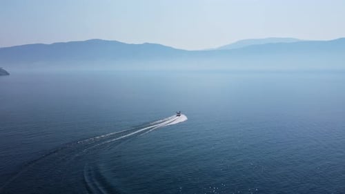 Speed boat driving fast in curves over deep, blue Okanagan Lake on a hot day during Canadian wildfir