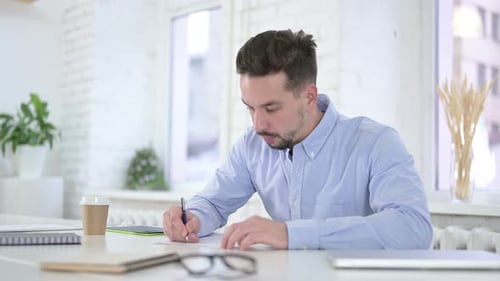 Man Writing at Desk in Modern Office
