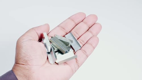 Hand Holding Shiny Metal Staples on White Background