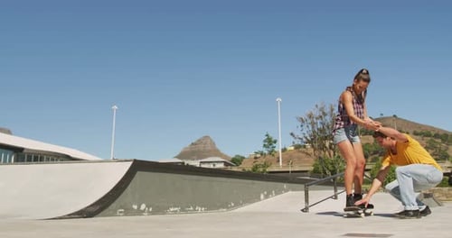 Woman Learning to Skateboard with Friend in Skatepark