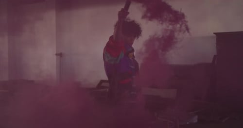 Mixed race man holding purple flare walking through an empty building