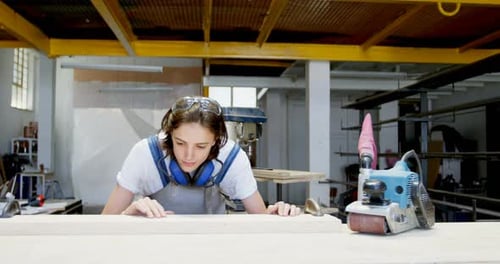 Woman Inspecting Wood on Workbench in Workshop