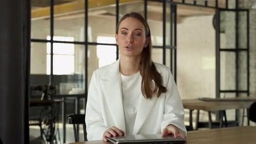 Woman in Office Talks to Camera at Desk