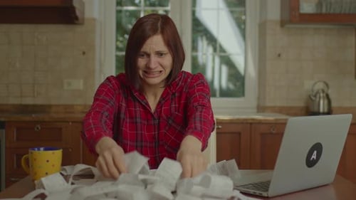 Frustrated 30s Woman is Upset with Big Expenses Checking Store Receipts Sitting at the Table in the