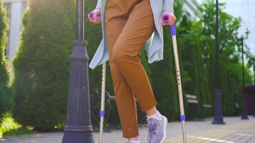 Unrecognizable Disabled Woman with an Injury on Crutches Walking in the Park Sunny Slow Mo