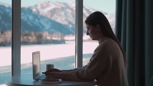 Woman Works at Laptop Overlooking Snowy Mountains