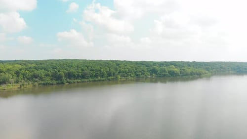vol avant de Drone vers un horizon et une limite d'arbres au-dessus d'un lac avec des feuilles vert vif avec du pu blanc