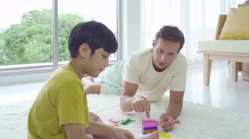Dad and son playing jigsaw puzzle game toy, building colorful blocks tower together