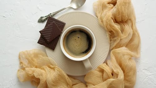 Taza de café negro con chocolate negro como guarnición. Colocado sobre una mesa de cocina