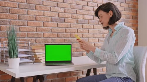 Woman Using Mobile Phone at Desk with Laptop
