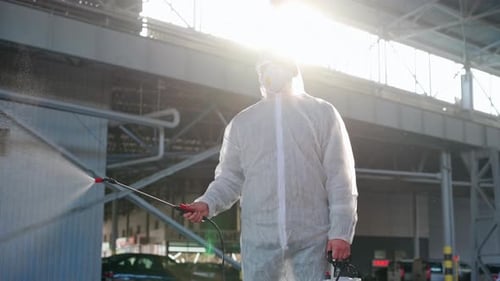 Worker in Suit Sprays Disinfectant in Bright Industrial Space