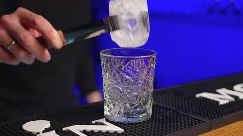 Bartender Adds Ice Cubes to the Glass in Slow Motion Making the Cocktail at the Bar Counter Blue
