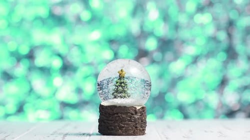 Closeup of Snowflakes Swirling Around a Christmas Tree Inside a Glass Ball