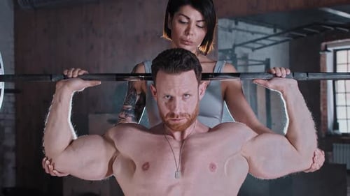 Attractive Couple Training in the Gym Athletic Man Pumping His Hands Muscles with a Dumbbell and