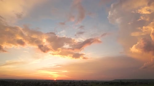 Dramatic moody sunset landscape with puffy clouds lit by yellow setting sun and blue sky.