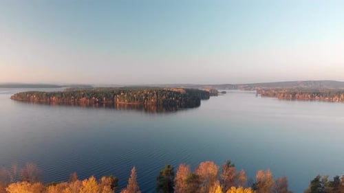 Revealing beautiful yellow trees moving back from a high up view over a calm lake with green islands