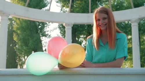 Smiling Girl Holding Balloons in an Urban Park