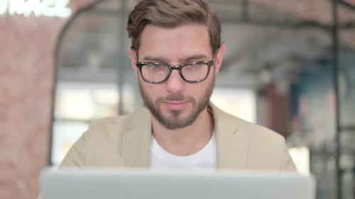 Nahaufnahme eines jungen Mannes mit Laptop, der in die Kamera schaut