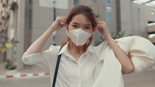 Businesswoman wear face mask smiling and looking at camera while happy alone outdoors in city